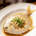 Two whole pomfret with golden fins arranged on crushed ice with lemon