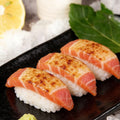Torched tuna nigiri sushi arranged on dark slate with shiso leaf and lemon