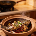 Braised grouper pieces simmering in a clay pot with spring onion